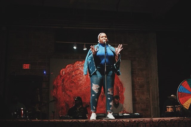 Singer performing on stage with red backdrop